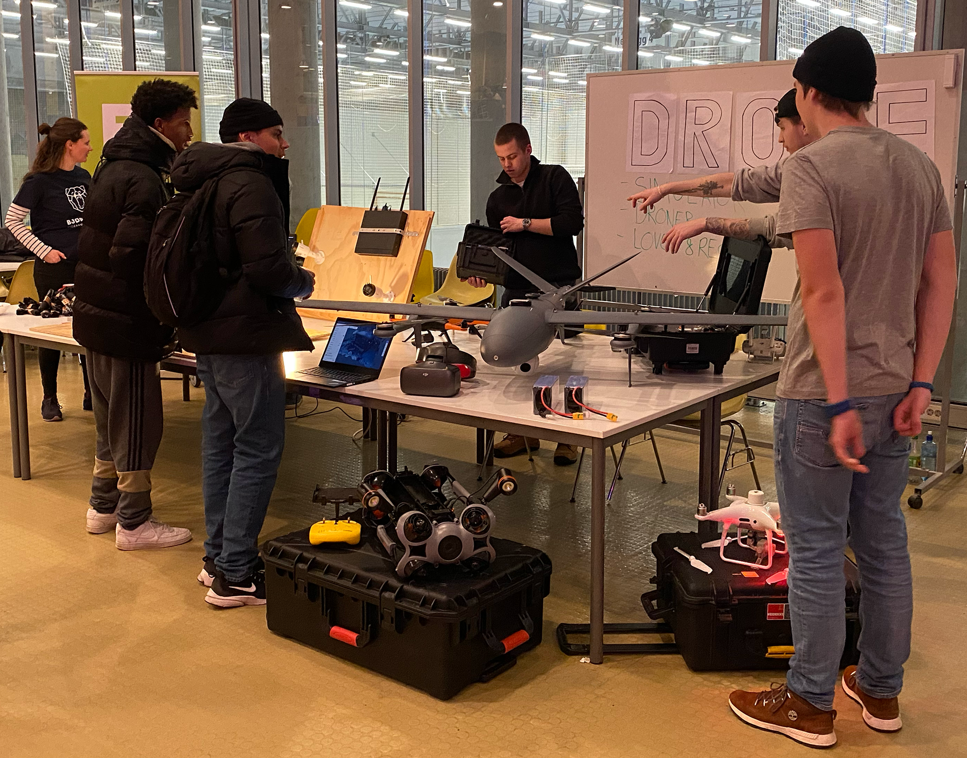 En gruppe mennesker som står rundt et bord med en bærbar datamaskin og en hvit tavle