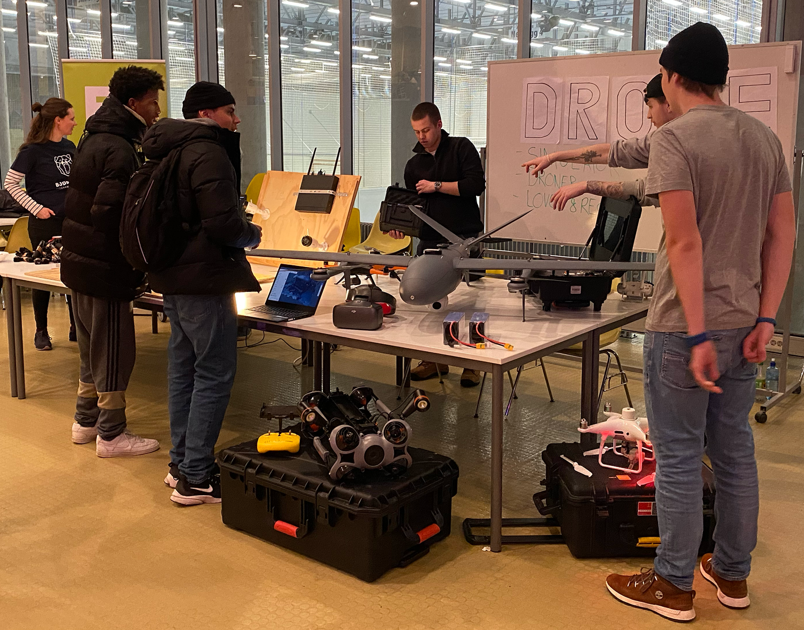 En gruppe mennesker som står rundt et bord med en bærbar datamaskin og en hvit tavle