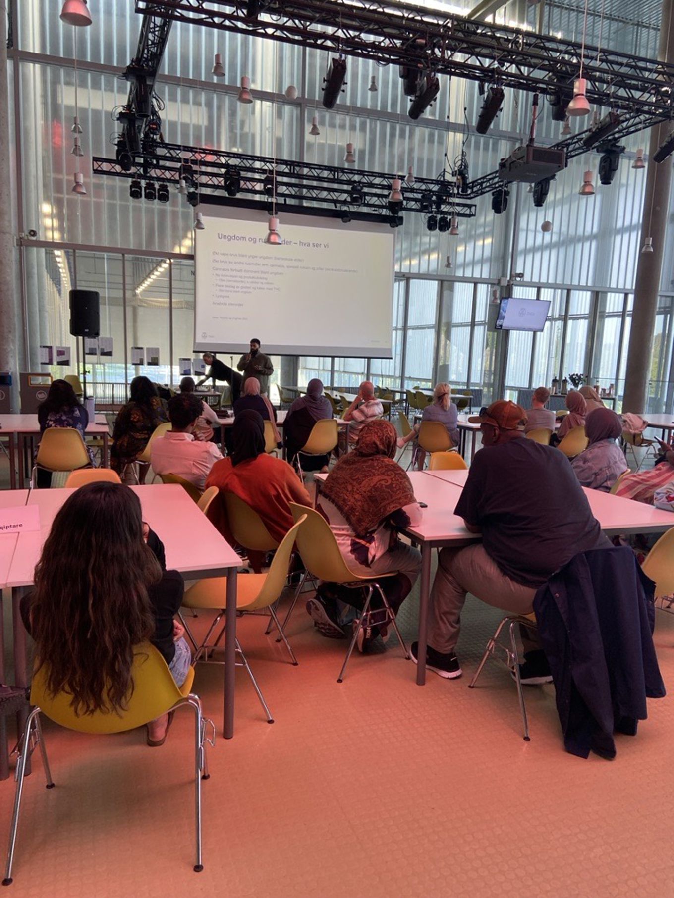 En gruppe mennesker som sitter i et rom med en projektorskjerm